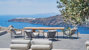 Una terraza con mesa y sillas de madera, con vistas a un paisaje costero con montañas y el mar.