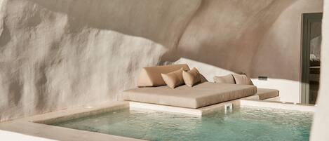 A modern spa area with a beige sofa and pillows by a pool.