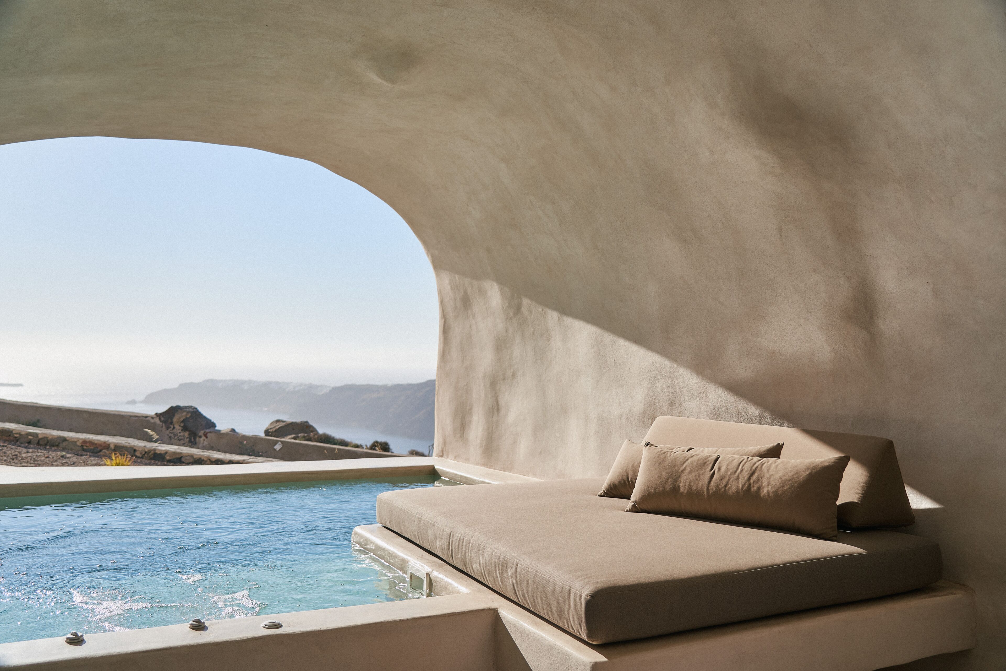 A modern, minimalist room with a large window overlooking a pool and a scenic view of mountains.