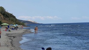 A beach with people, umbrellas, and a rocky coastline.