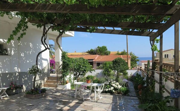 A covered outdoor area with a pergola, stone flooring, and potted plants.