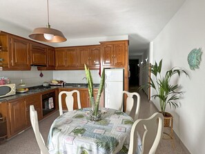 A kitchen with wooden cabinets, a microwave, a refrigerator, and a dining table with chairs.