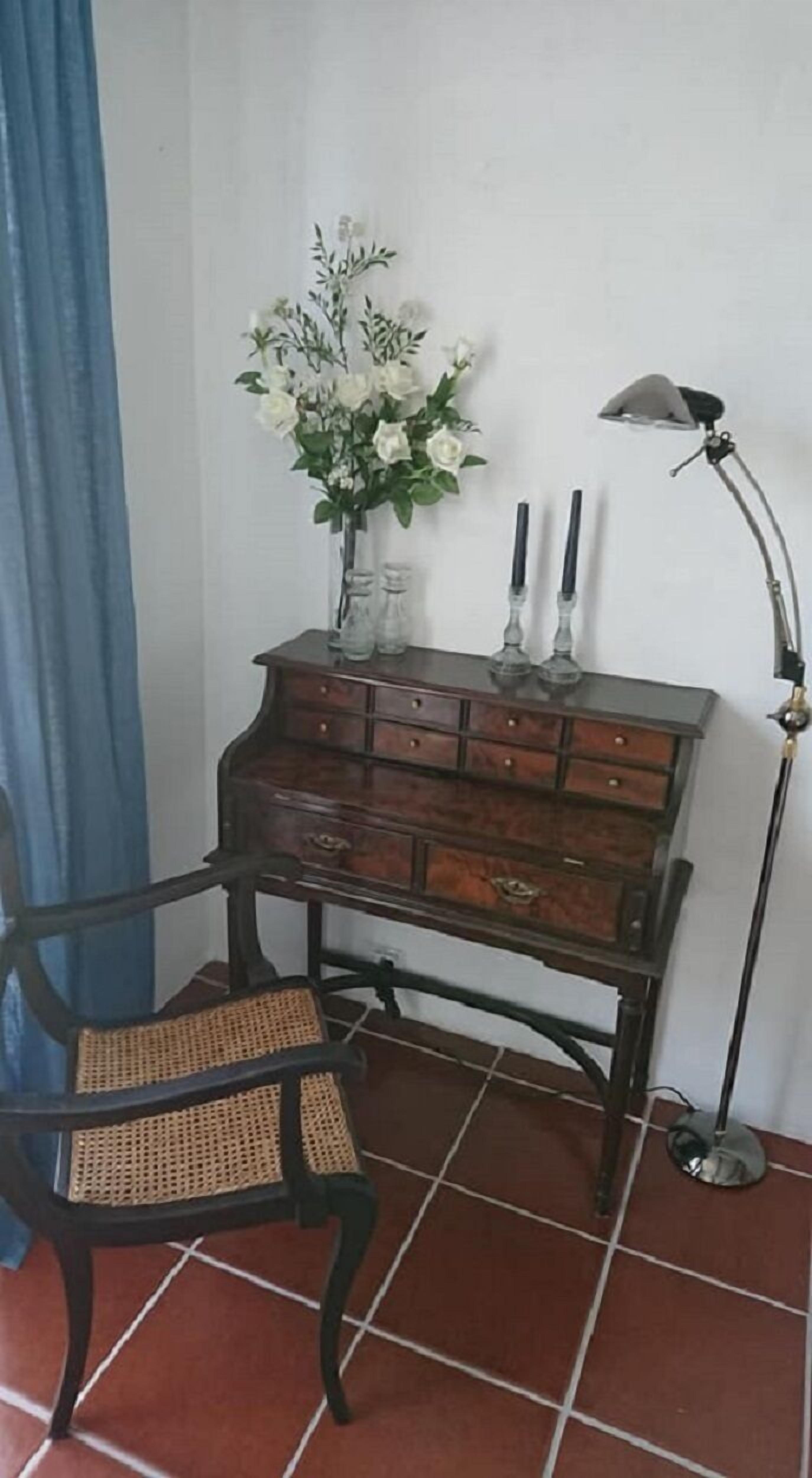 A wooden dresser with multiple drawers, a vase with white flowers, and a floor lamp.