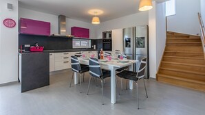 Eine moderne Küche mit Essbereich, inklusive einer zentralen Kochinsel, Pendelleuchten und einer Treppe.