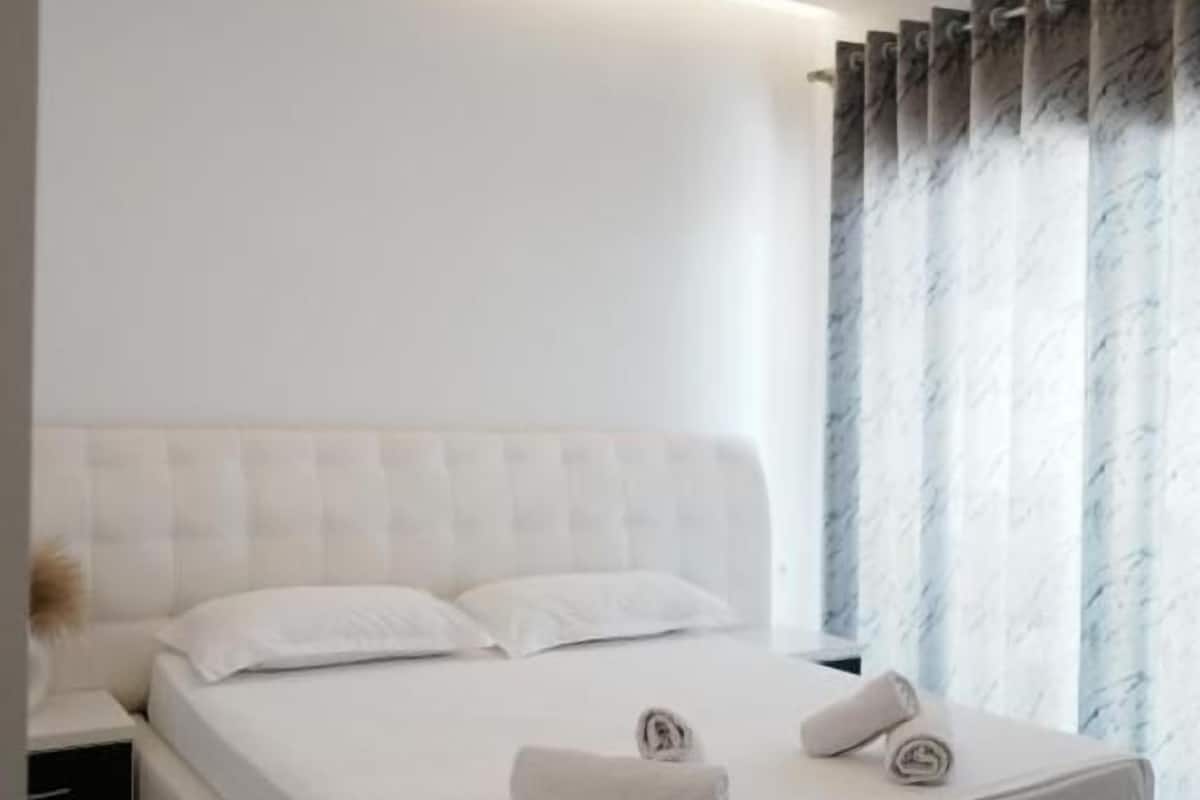 A modern bedroom with a large bed, a nightstand, and a window with curtains.