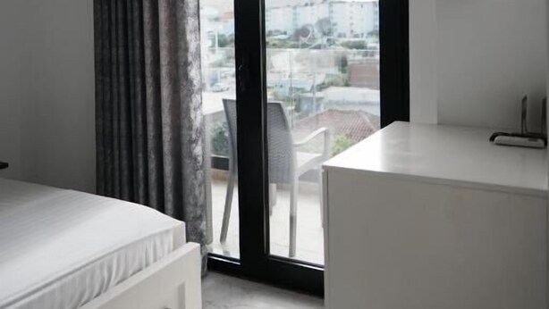 A modern bedroom with a bed, a white dresser, a sliding glass door to a balcony, and an air conditioning unit. - Eos ApartHotel (Ksamil)