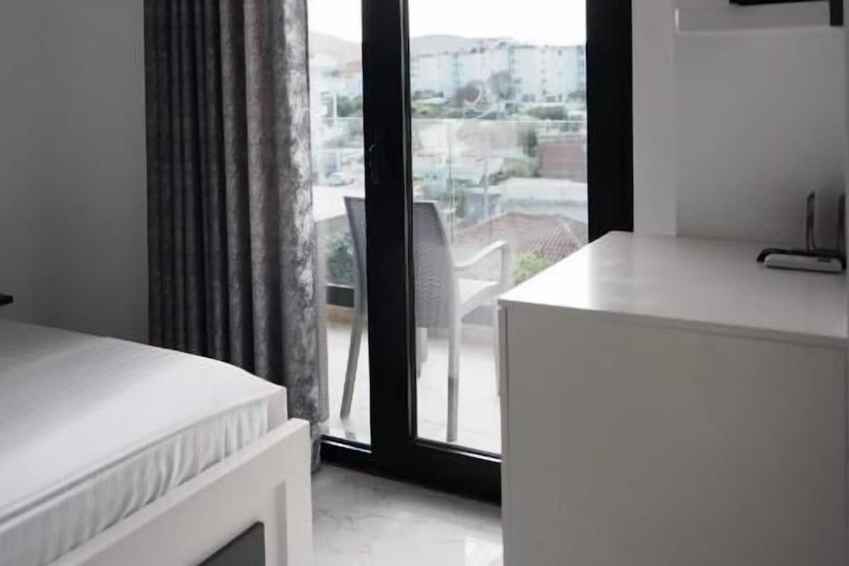 A modern bedroom with a bed, a white dresser, a sliding glass door to a balcony, and an air conditioning unit.