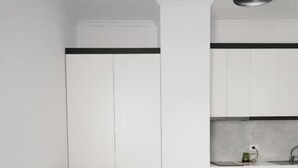A modern kitchen with white cabinets, a grey sofa, and a pendant light. - Eos ApartHotel (Ksamil)