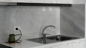 A kitchen with white cabinets, a stainless steel sink, and a green kettle. - Eos ApartHotel (Ksamil)