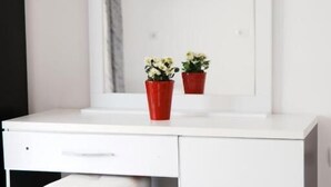 A white desk with a flat-screen TV mounted above it, two red flower pots on the desk, and a black and white ottoman under the desk. - Eos ApartHotel (Ksamil)