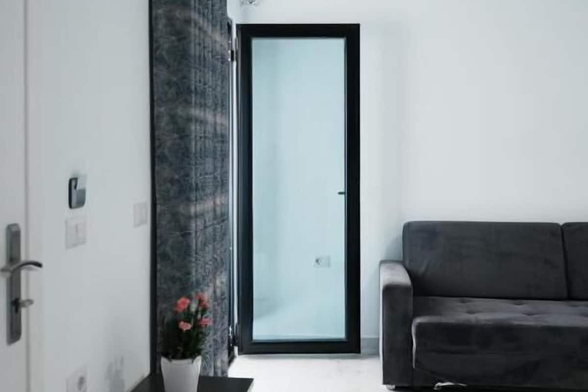 A modern living room with a grey sofa, a white cabinet with a potted plant, and a glass door leading to a balcony.