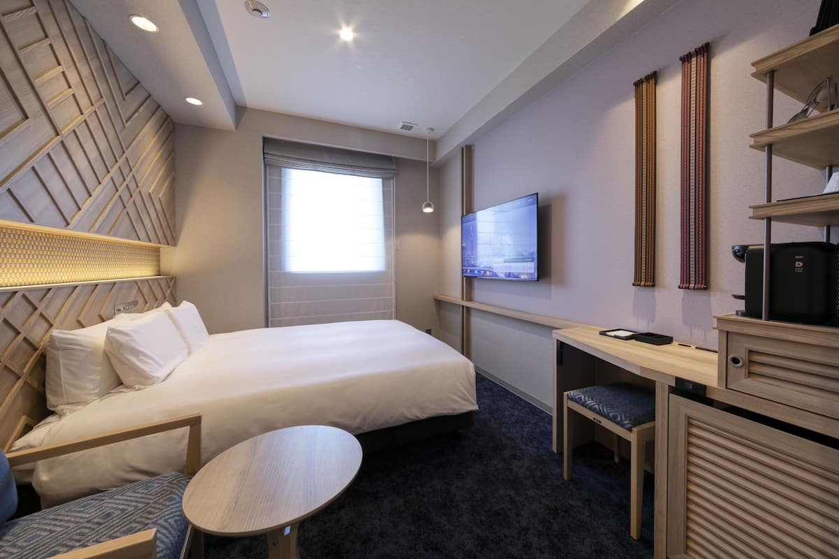 Ein Hotelzimmer mit einem Bett, einem Schreibtisch, einem Stuhl, einem Fernseher und einem Fenster.