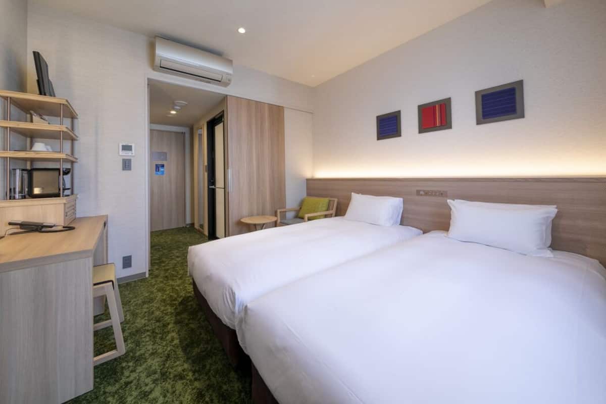 Ein Hotelzimmer mit zwei Betten, einem Schreibtisch, einem Stuhl und einem kleinen Tisch.