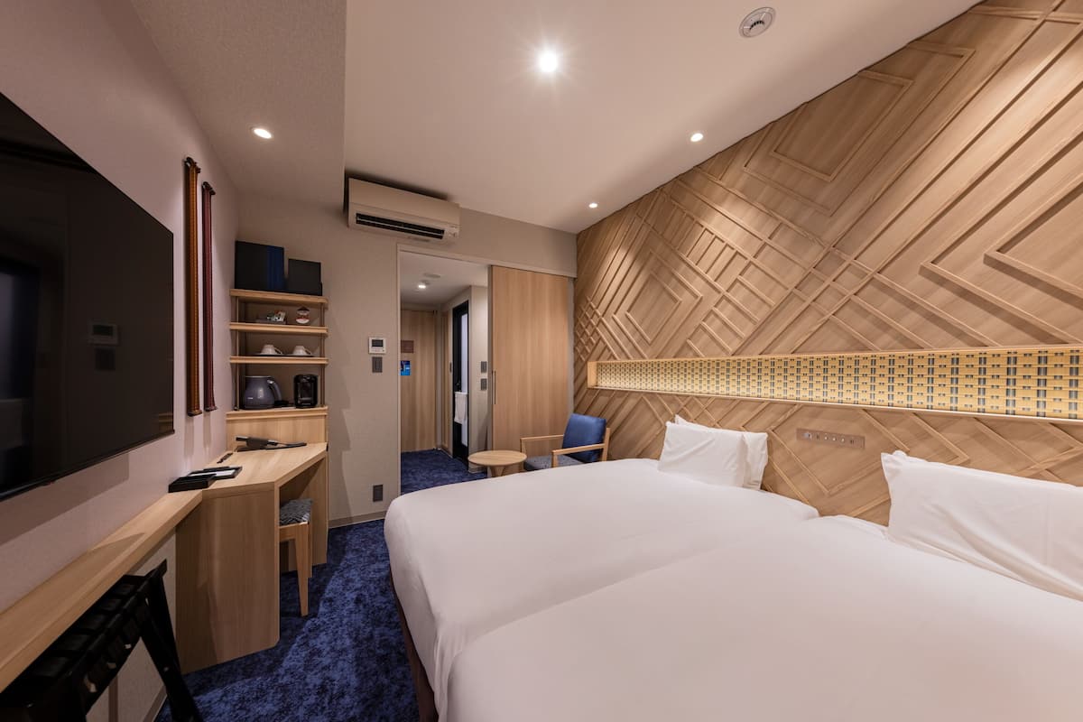 Ein Hotelzimmer mit einem großen Bett, einem Schreibtisch, einem Sessel, einem Fernseher und einer Wand mit Holzvertäfelung.
