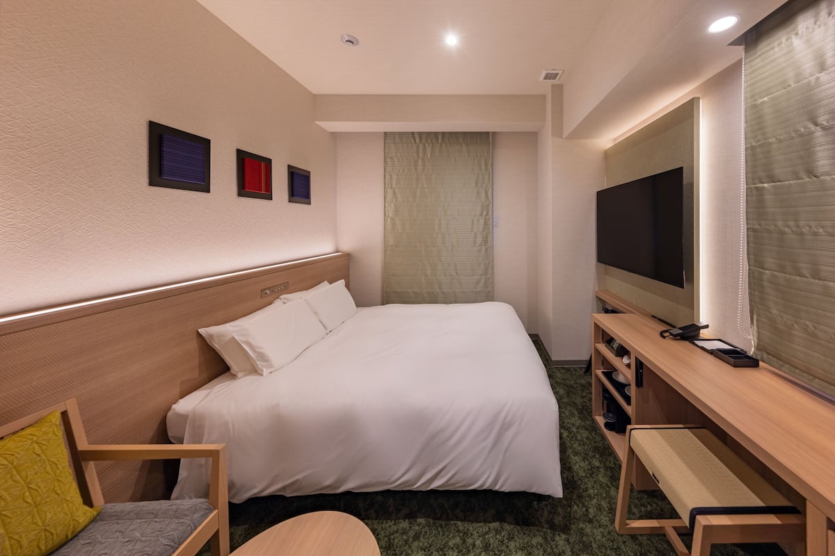Ein Hotelzimmer mit Bett, Schreibtisch, Stuhl, Fernseher und einem Fenster mit Vorhängen.