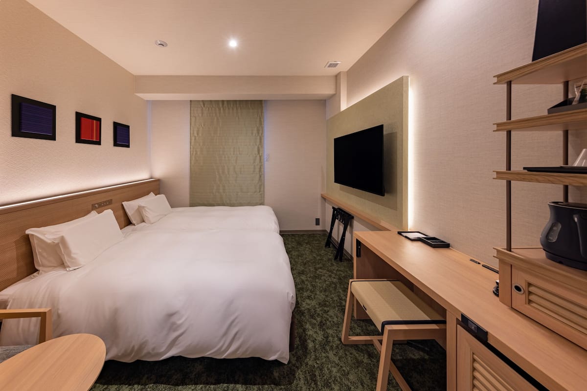 Ein Hotelzimmer mit einem Bett, einem Schreibtisch, einem Fernseher und einem Regal mit Gegenständen.