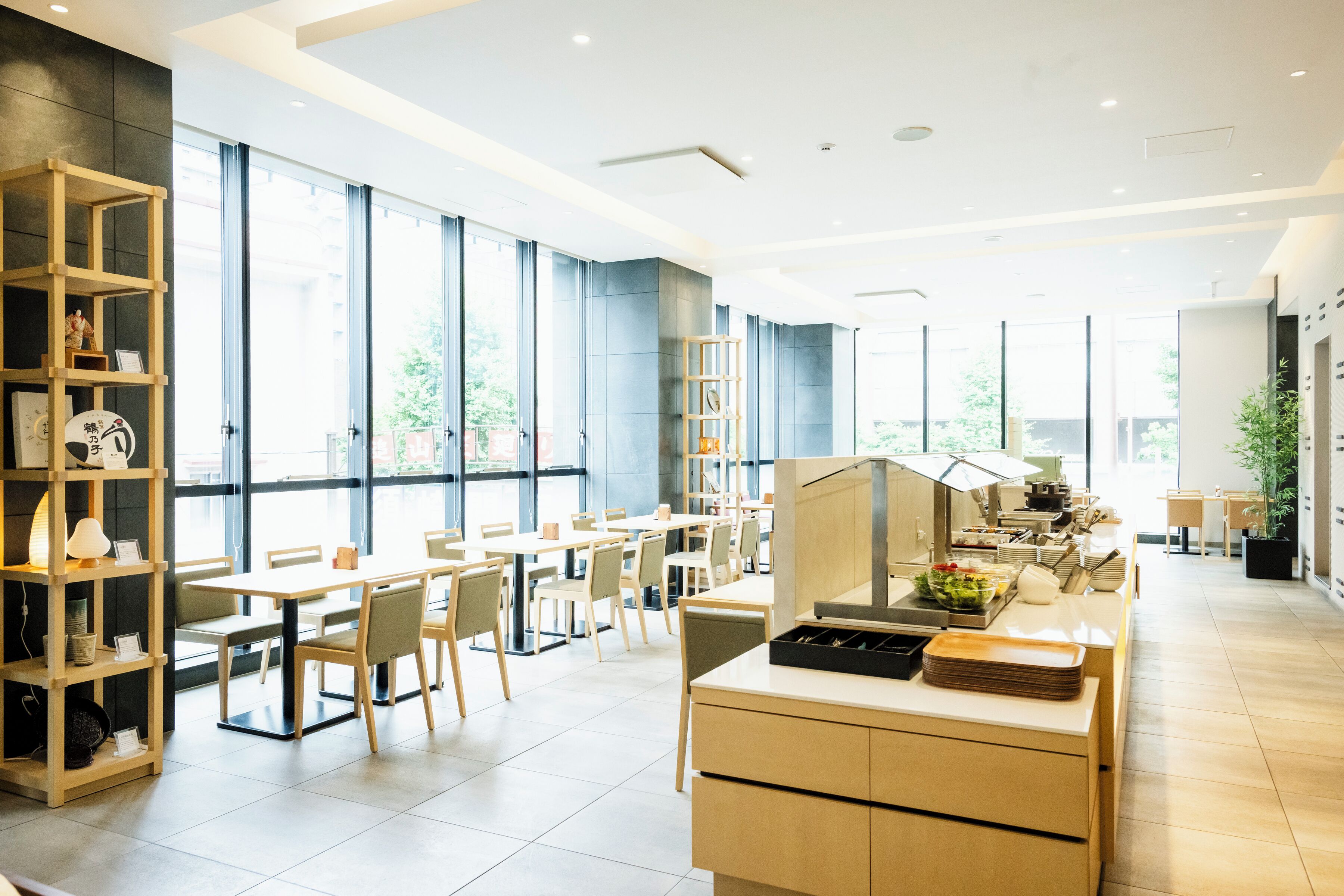 Un'area pranzo moderna con tavoli e sedie in legno, un banco buffet e ampie finestre che lasciano entrare luce naturale.