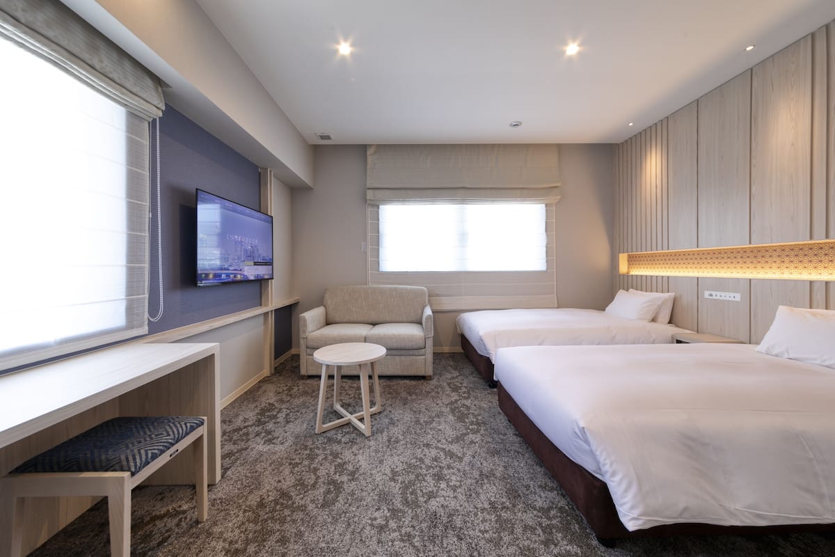 Ein Hotelzimmer mit Bett, Schreibtisch, Sessel, Fernseher und Fenster.