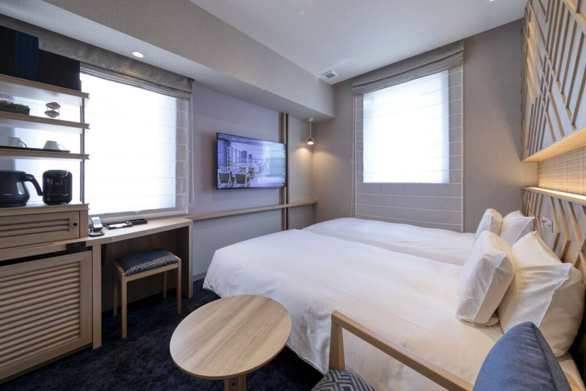 Ein Hotelzimmer mit Bett, Schreibtisch mit Stuhl, Fernseher und Fenster.