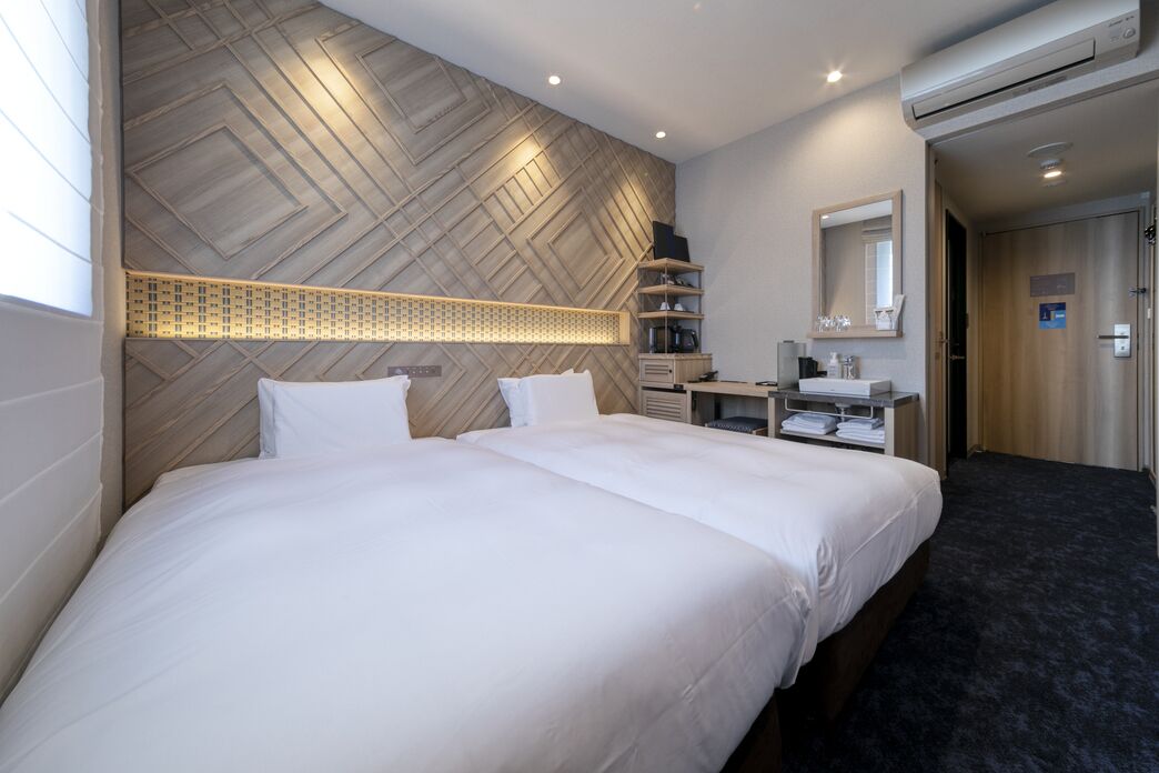 Quarto de hotel com uma cama grande, uma escrivaninha, um espelho e uma parede com padrão geométrico.