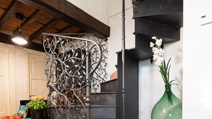 A modern kitchen with a black staircase, a green vase with flowers, and a table with fruits and books. - Villa "Il Grillo", privacy in the hills, private pool and panoramic view. (Toscana)
