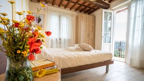 A bedroom with a bed, a bedside table with books and a vase of flowers, a wooden floor, and a balcony with a view. - Villa "Il Grillo", privacy in the hills, private pool and panoramic view. (Toscana)