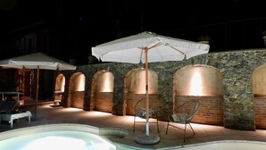 An outdoor pool area with stone walls and arched windows, surrounded by lounge chairs and umbrellas. - Villa "Il Grillo", privacy in the hills, private pool and panoramic view. (Toscana)