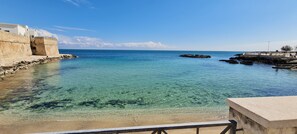 A coastal view with clear water, a stone wall, and a rocky outcrop.