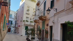 Une rue étroite, bordée de bâtiments des deux côtés, dont certains sont dotés de balcons et de plantes en pot.