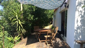 A wooden deck with a table and chairs, surrounded by greenery and a patterned canopy.