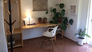 A corner room with a wooden desk, a white chair, a lamp, and several potted plants.