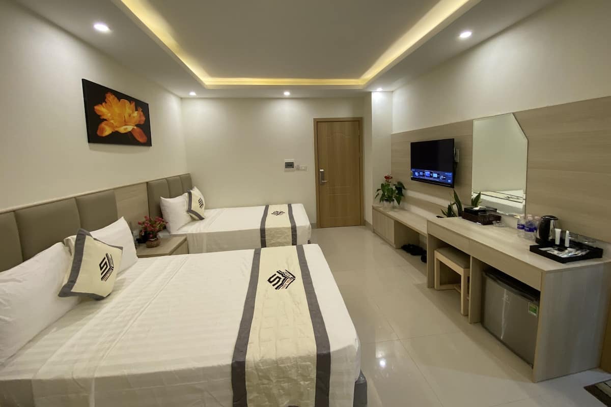 A hotel room with two beds, a TV, a desk, and a bathroom.