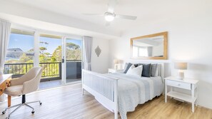 A bedroom with a bed, bedside tables, a desk, and a chair. There is a balcony with a view of the outdoors.