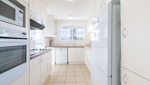 A modern kitchen with white cabinets, a built-in oven, a dishwasher, and a window providing natural light. - Albacore 6, 12-14 Ondine Close (Nelson Bay)