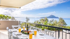 Une table dressée pour le dîner, avec vue sur la mer et une montagne en arrière-plan.