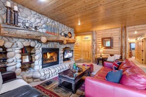 L’intérieur d’une cabane en rondins, avec une cheminée en pierre, un canapé en cuir et des murs en bois.