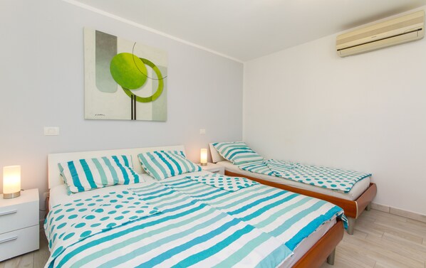 A bedroom with two beds, each with striped bedding, a nightstand with a lamp, and a wall-mounted air conditioner.