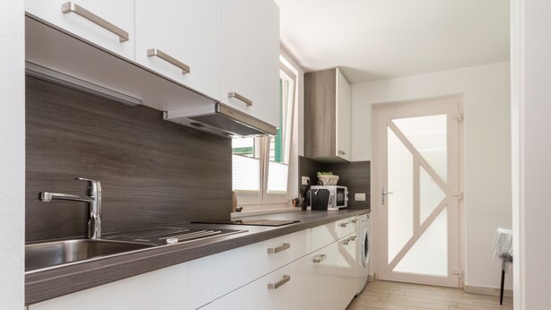 A modern kitchen with a stainless steel sink, white cabinets, and a dark backsplash. - Apartments Kolenc (Piran)