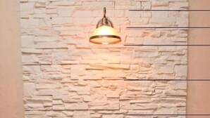 Uma área de refeições com parede de pedra ao fundo, luminária pendente e mesa com cadeiras.