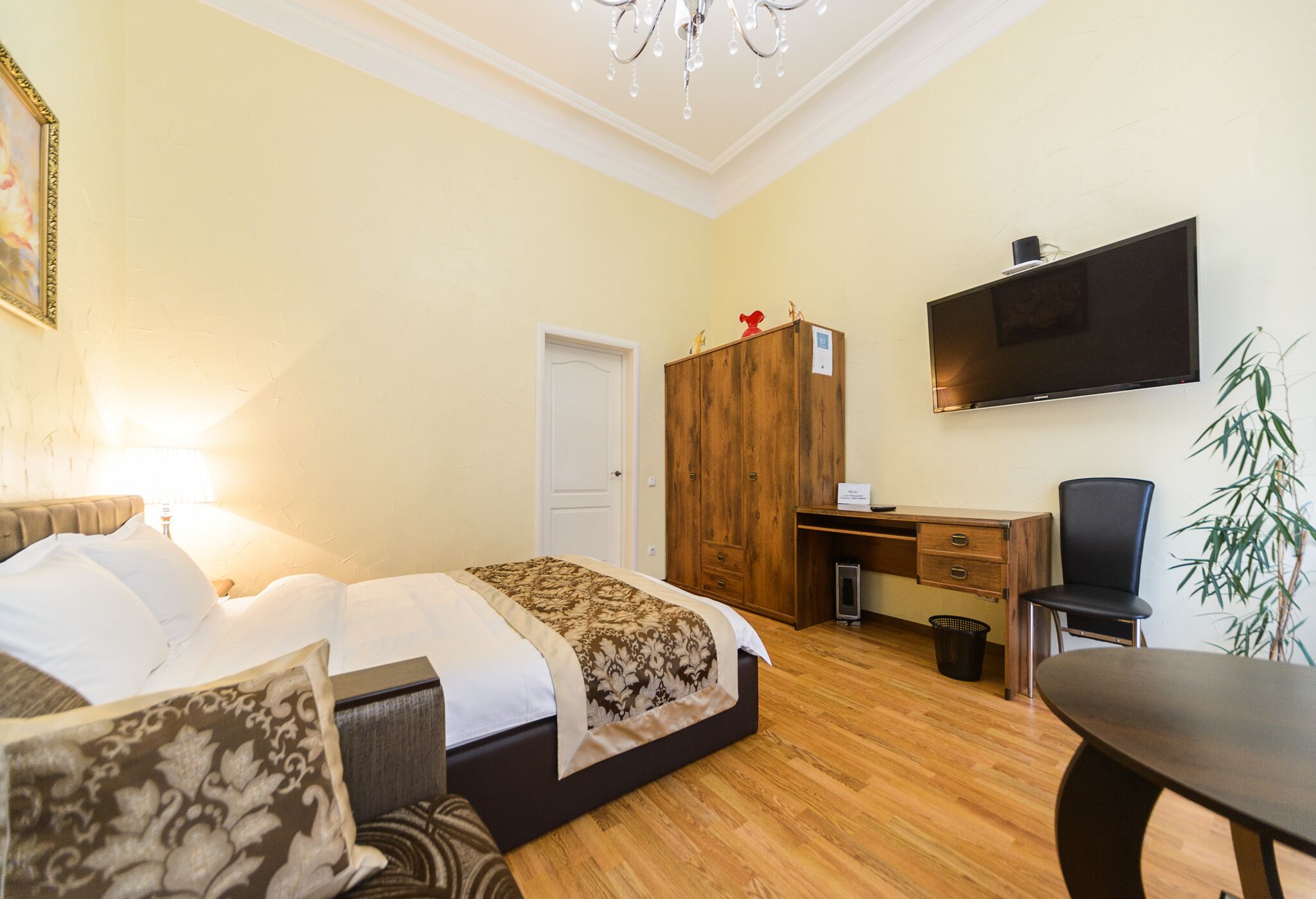 A hotel room with a bed, a desk, a chair, a TV, and a plant.