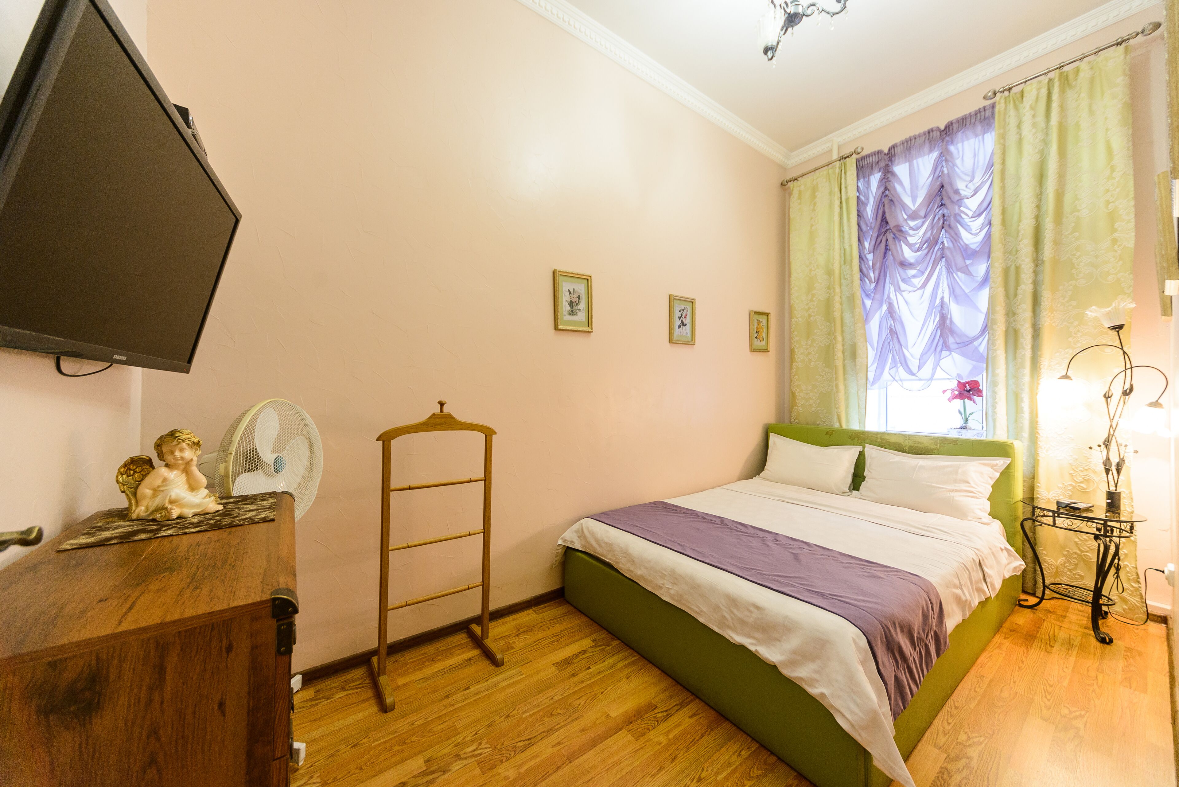 A bedroom with a bed, a dresser, a television, and a window with curtains.