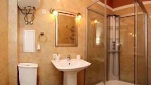 Casa de banho com lavatório de pedestal, sanita, cabine de duche em vidro e espelho com iluminação.