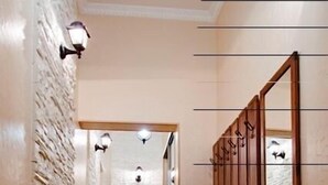 Um corredor com piso de madeira, parede de pedra de um lado e cômoda de madeira com espelho.