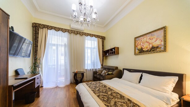 Quarto de hotel com uma cama grande, uma escrivaninha com cadeira, uma televisão na parede e um lustre.