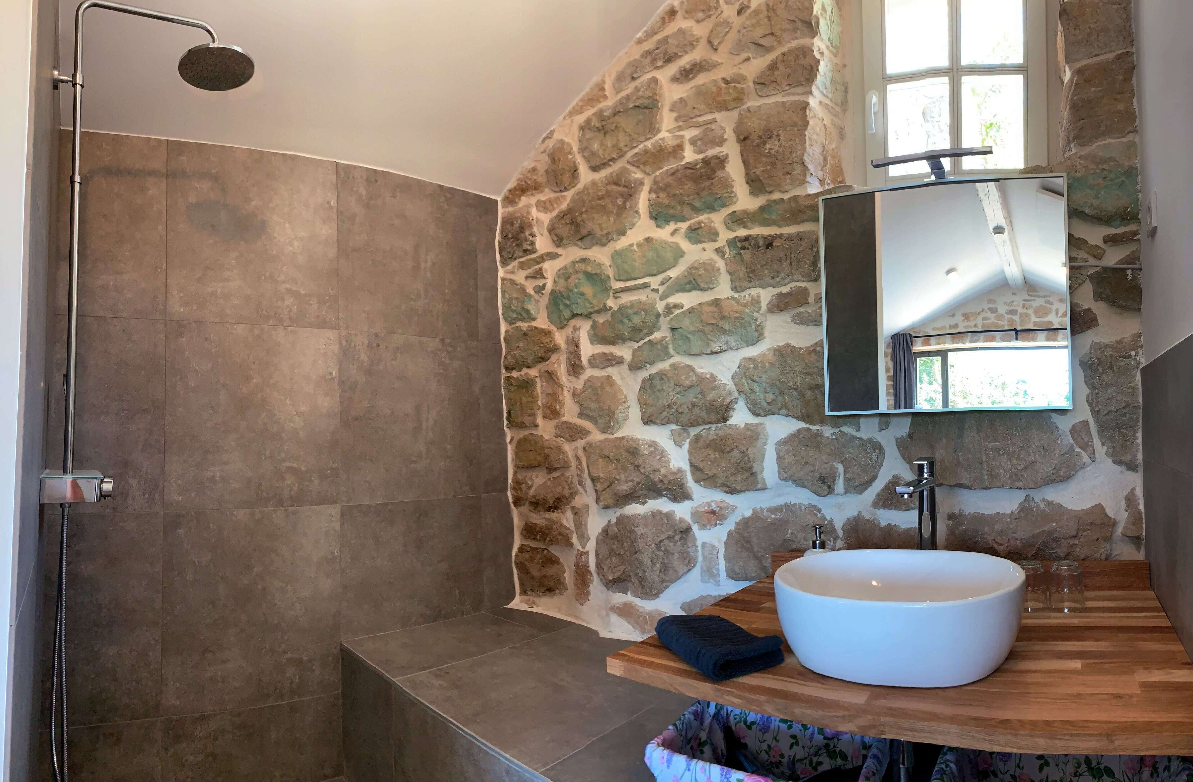 A bathroom with a stone wall, a large sink, and a shower.