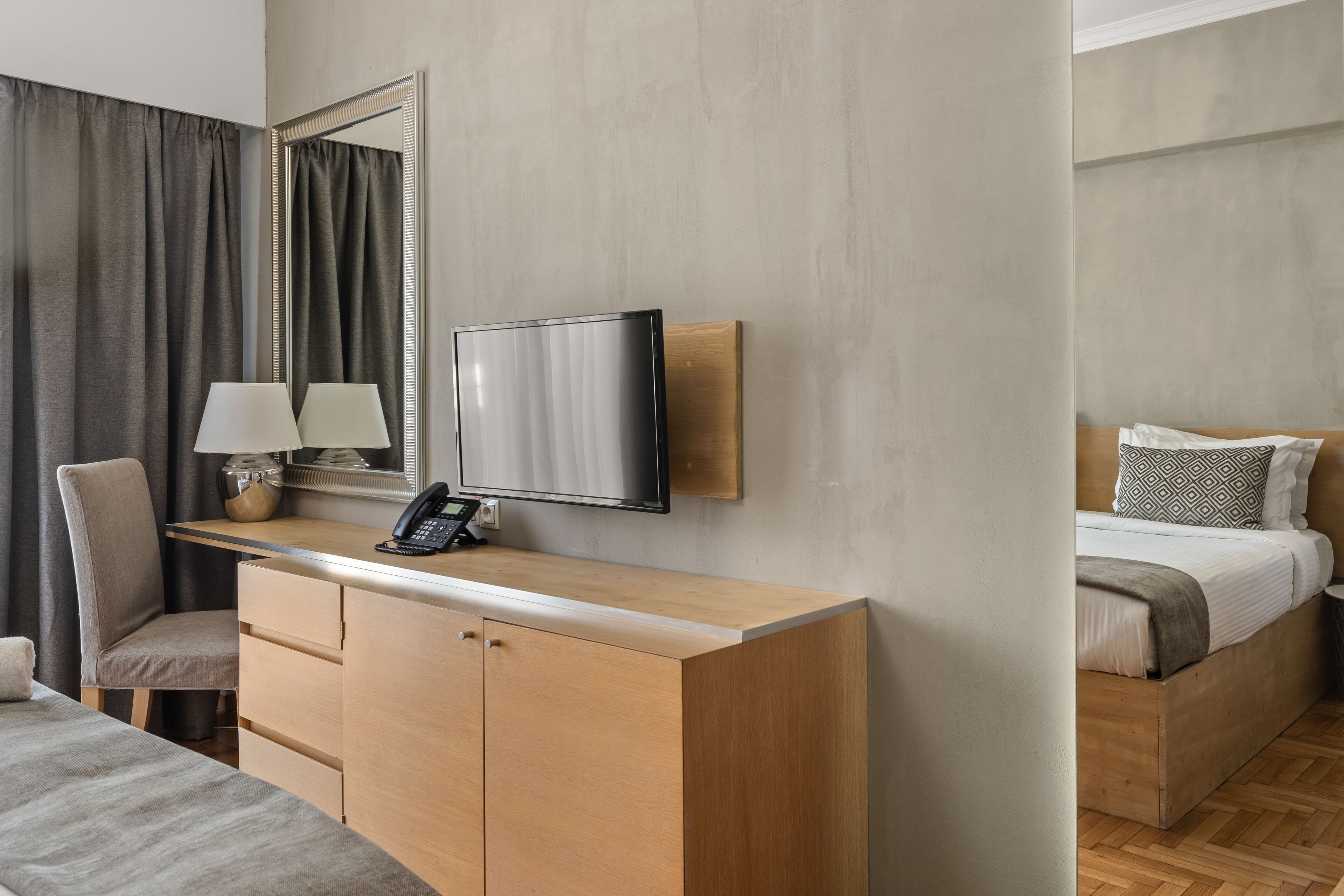 Une chambre d’hôtel avec un bureau en bois, un téléviseur à écran plat, une chaise, un lit avec des oreillers à motifs et un grand miroir.