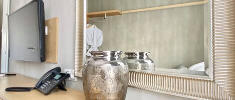 A wooden desk with a telephone, a large mirror with a decorative frame, and two metallic vases.