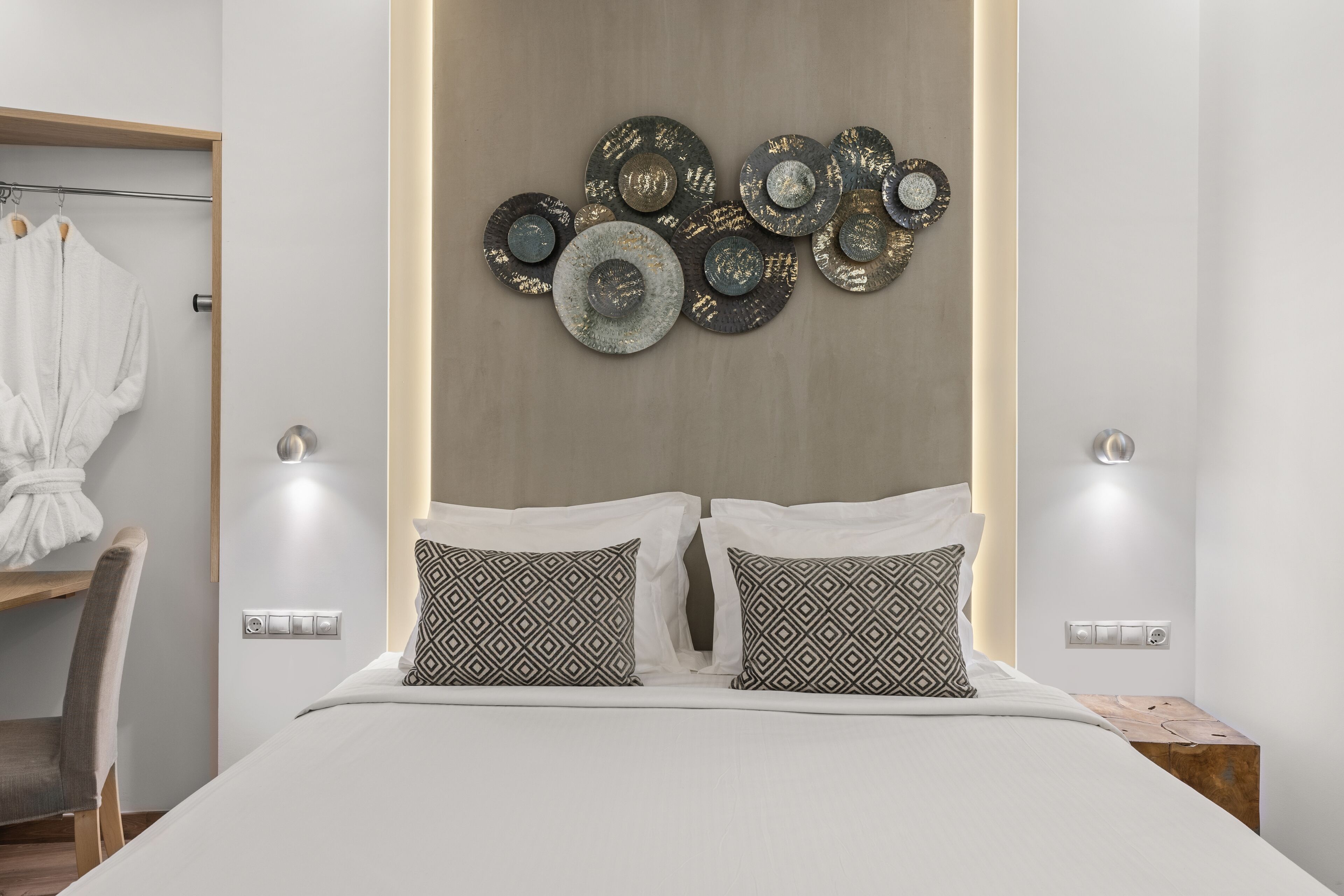 A modern bedroom with a bed, patterned pillows, a wall-mounted decorative piece, bedside lamps, and a wooden nightstand.