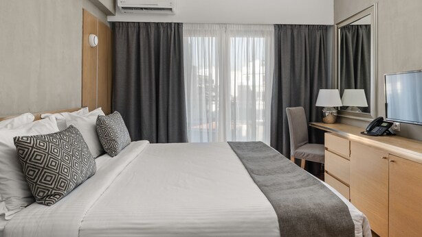 Ein Hotelzimmer mit Bett, Schreibtisch, Lampe, Telefon und Fernseher.