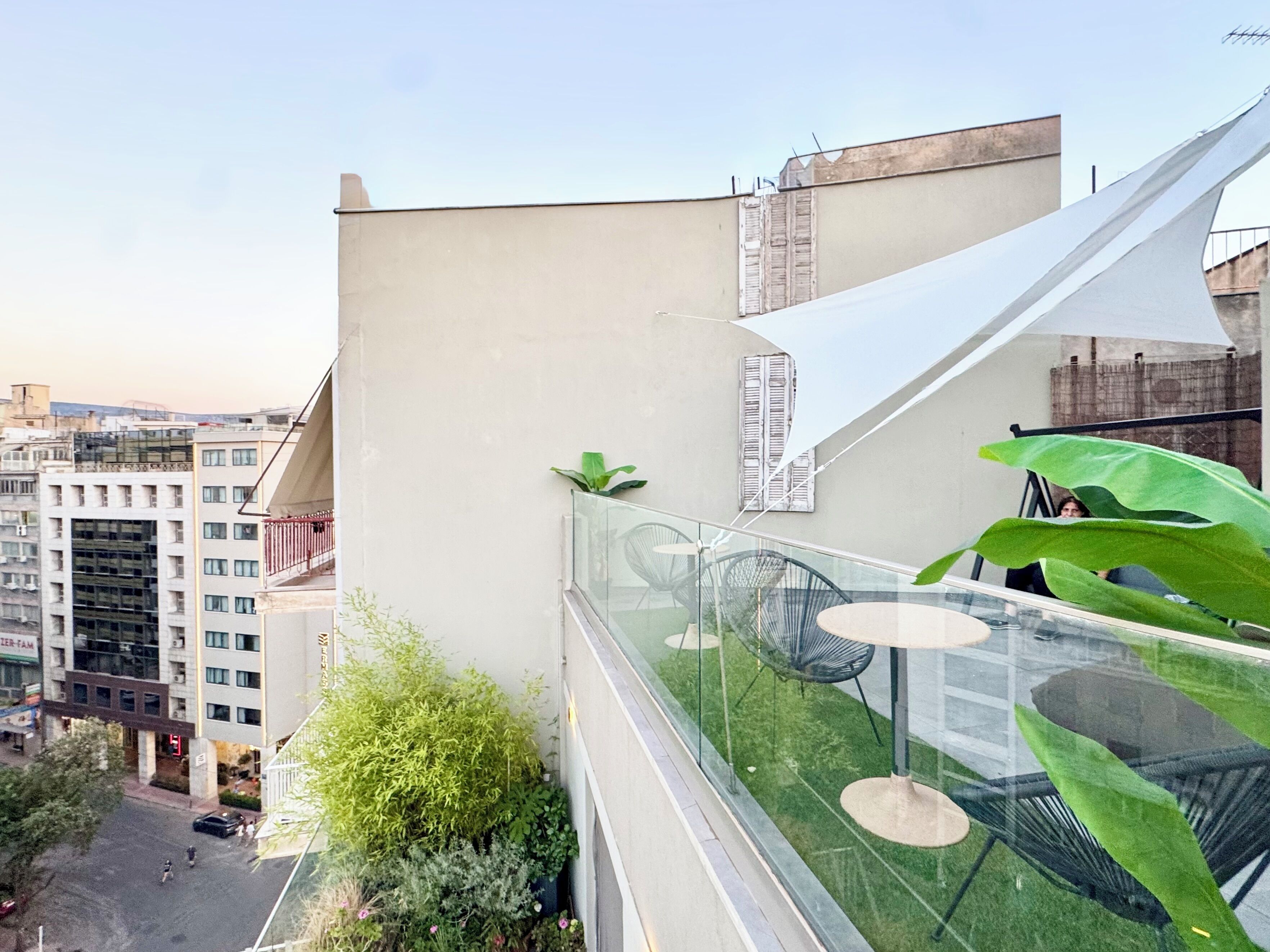 Terraço no telhado com guarda-corpos de vidro, área de estar ao ar livre e vista para a cidade.